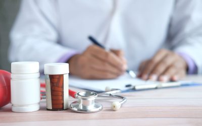 Close-up of prescription bottles and stethoscope with a blurred background of a person writing