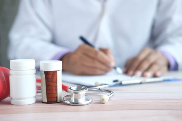 Close-up of prescription bottles and stethoscope with a blurred background of a person writing