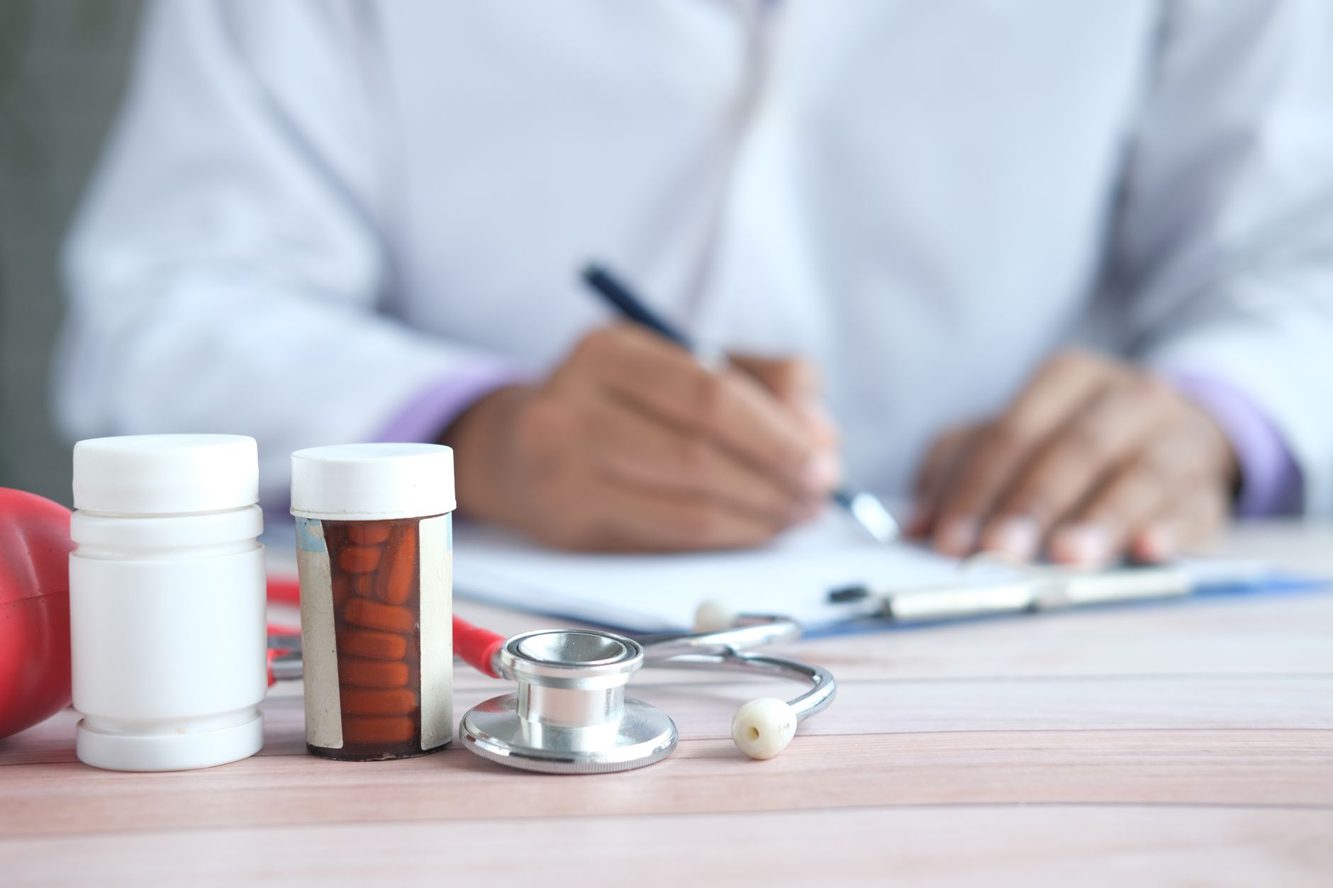 Close-up of prescription bottles and stethoscope with a blurred background of a person writing